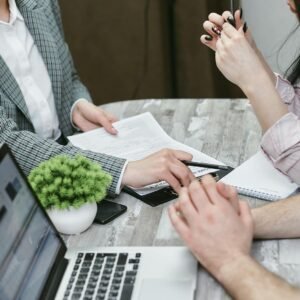 Professional meeting discussing business agreements with laptops and documents on a rustic table.